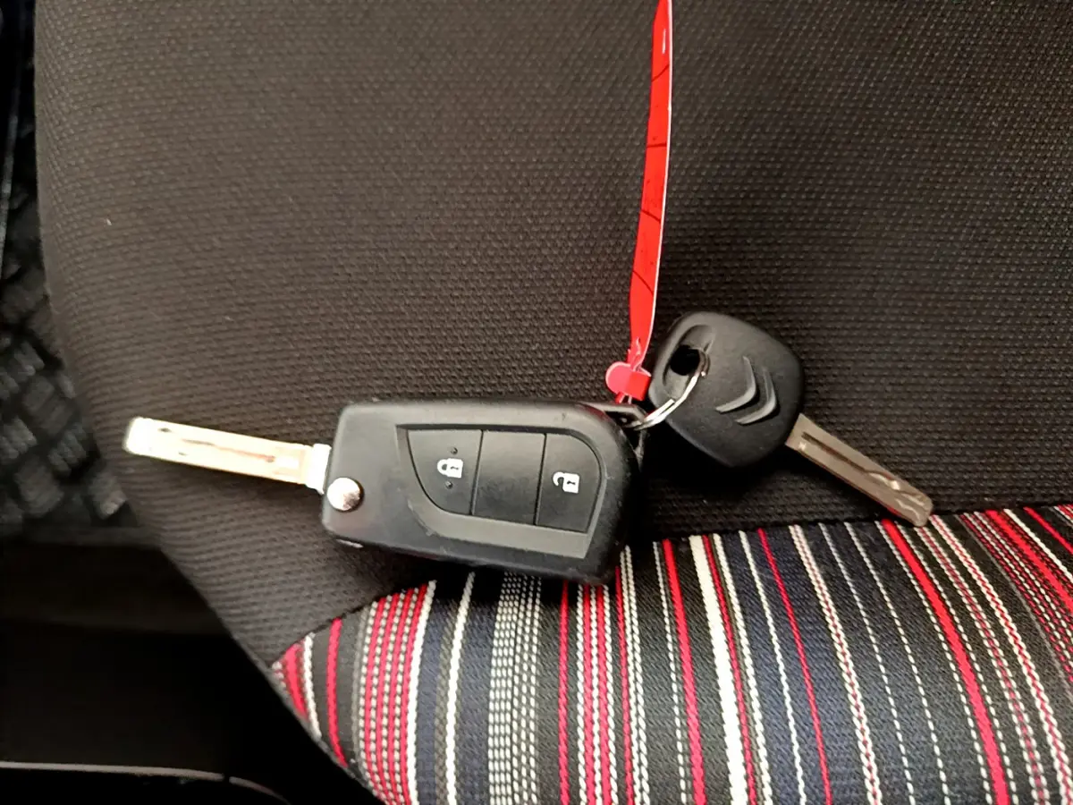 Clé de voiture Citroën posée sur un siège tissu noir avec bandes rouges, blanches et grises, vue rapprochée intérieure.