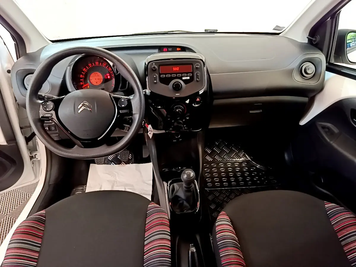 Vue intérieure avant de la Citroën C1 blanche, volant multifonction, tableau de bord noir avec écran central rouge.