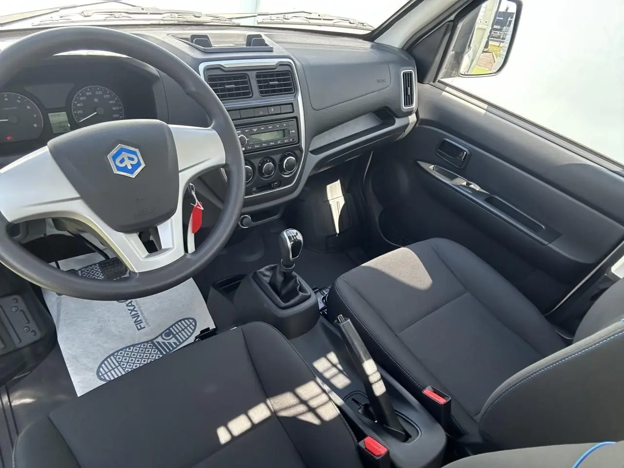 Intérieur du Piaggio Porter 2024 vu côté conducteur, volant avec logo bleu, tableau de bord simple et sièges noirs.