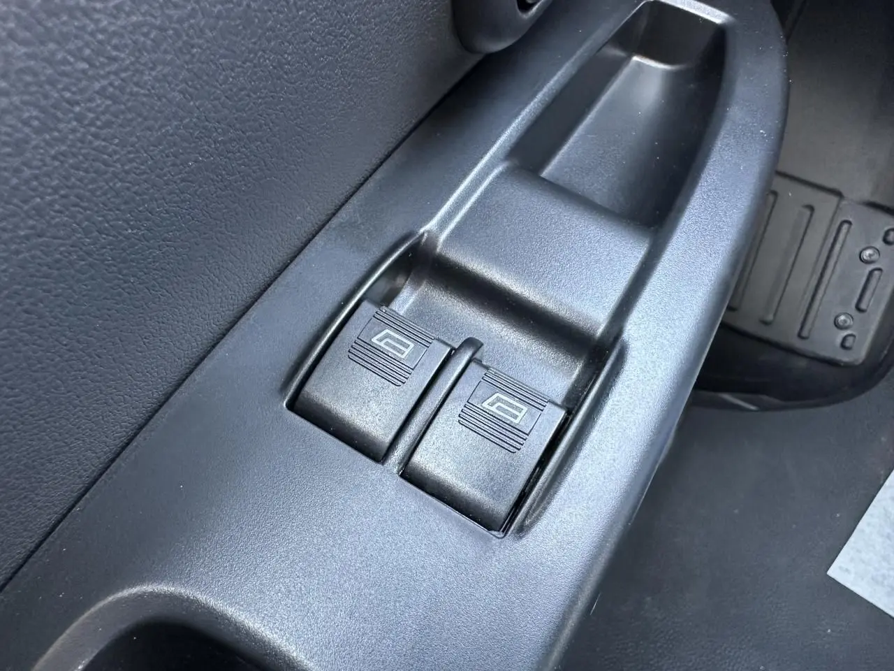 Gros plan sur les commandes de lève-vitres électriques côté conducteur du Piaggio Porter blanc, intérieur noir.