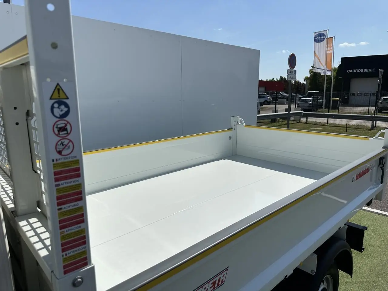 Benne blanche vue en 3/4 arrière droit du Piaggio Porter 2024 avec plateau de chargement long et bordures jaunes.