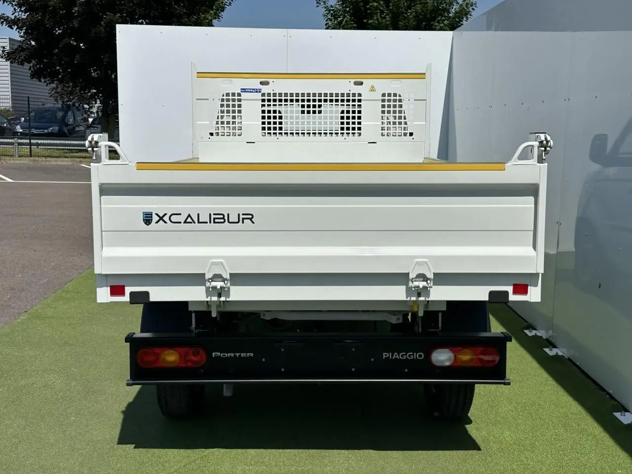 Vue arrière d'un Piaggio Porter blanc avec benne longue et marquage Xcalibur sur fond extérieur clair.