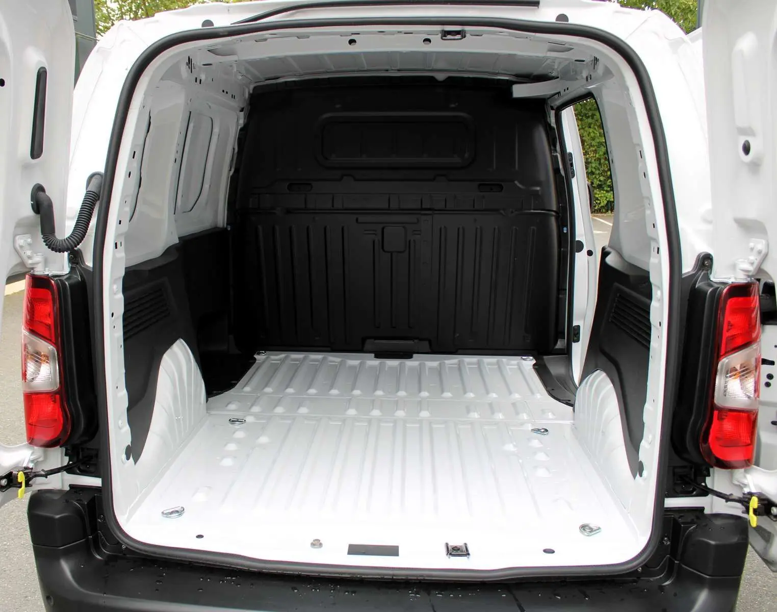 Vue arrière du Peugeot Partner Fourgon blanc 2025 avec portes ouvertes montrant l'espace de chargement vide et les feux arrière rouges.