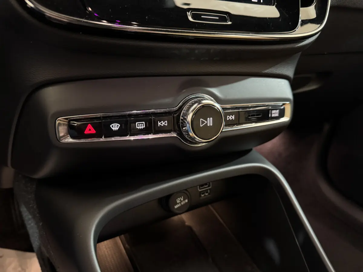 Gros plan sur la console centrale noire du Volvo XC40 Recharge T5 2021, avec commandes audio et prise 12V visibles.