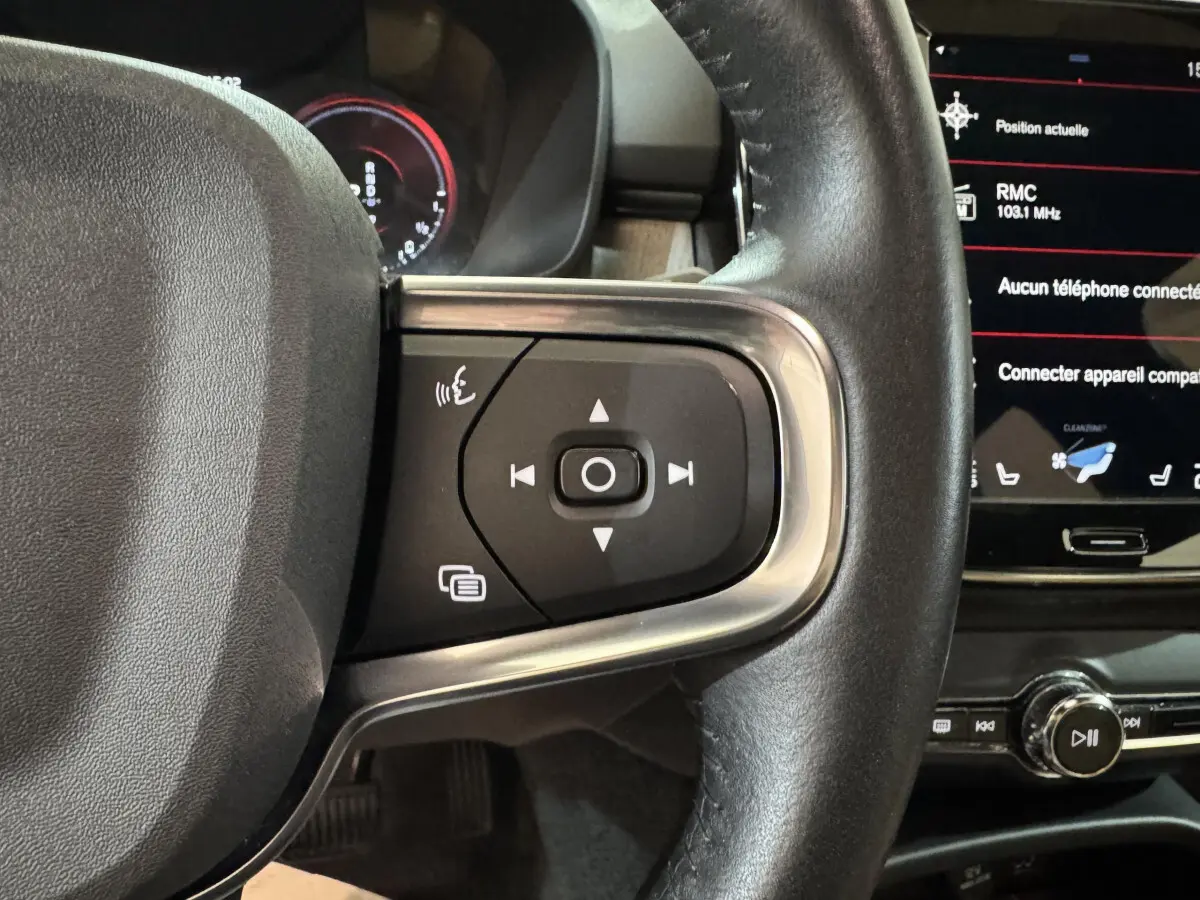 Gros plan sur le côté droit du volant noir en cuir du Volvo XC40 Recharge T5, avec commandes multifonctions et écran tactile visible.