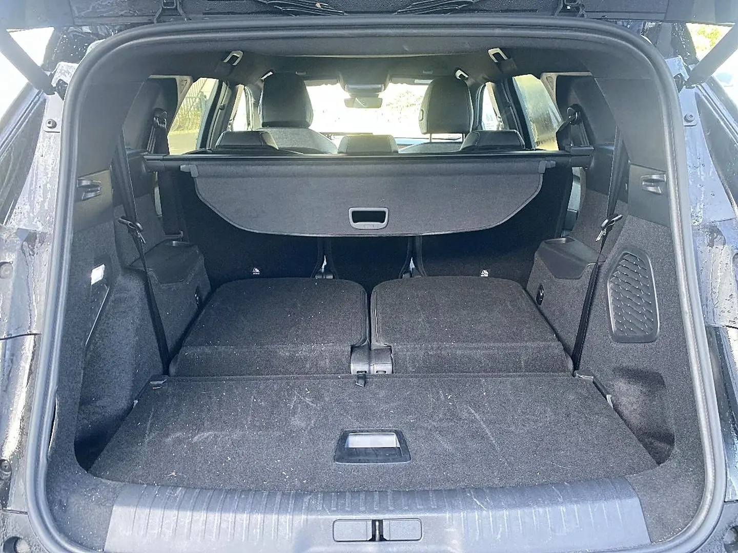 Coffre ouvert d’un Peugeot 5008 noir, vue arrière montrant les sièges rabattus et le cache-bagages déployé.