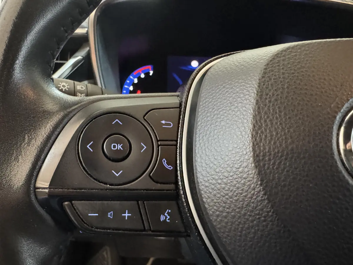 Gros plan sur le volant cuir noir de la Toyota Corolla Hybride 122h, avec commandes multifonctions et affichage digital partiel.