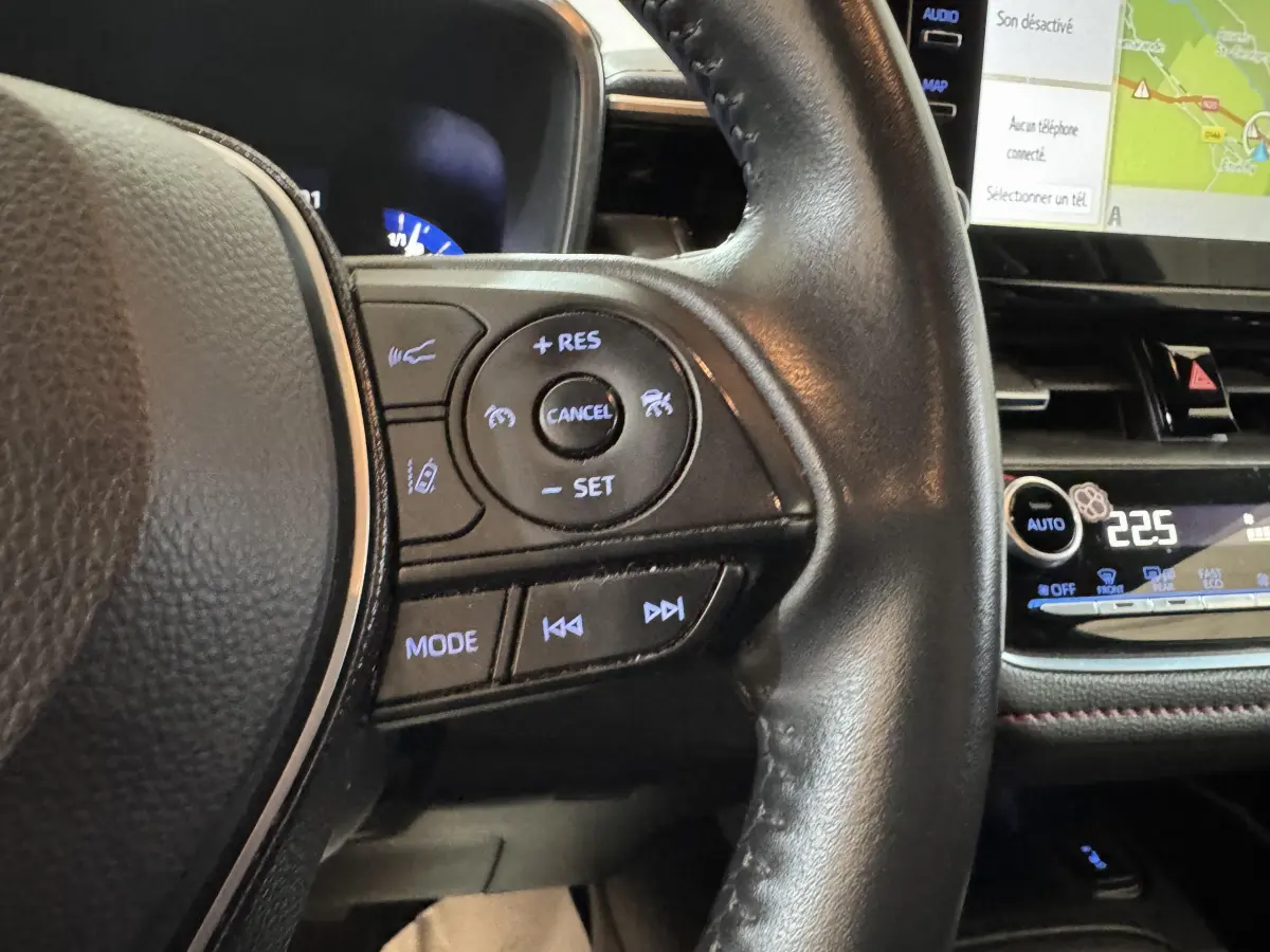 Gros plan sur le volant cuir noir de la Toyota Corolla Hybride 122h 2021, avec commandes multifonctions et écran tactile visible.