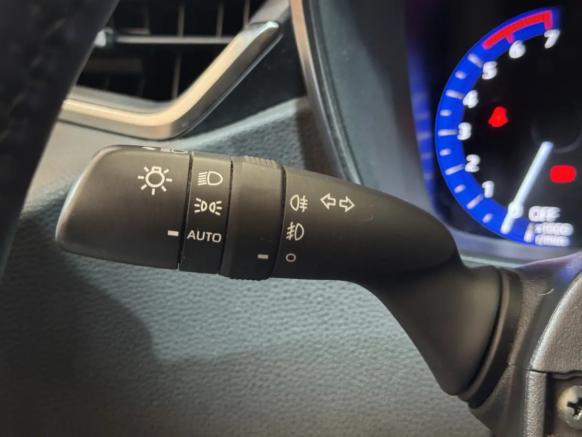 Gros plan sur la commande des phares et clignotants à gauche du volant dans l'habitacle d'une Toyota Corolla gris clair.