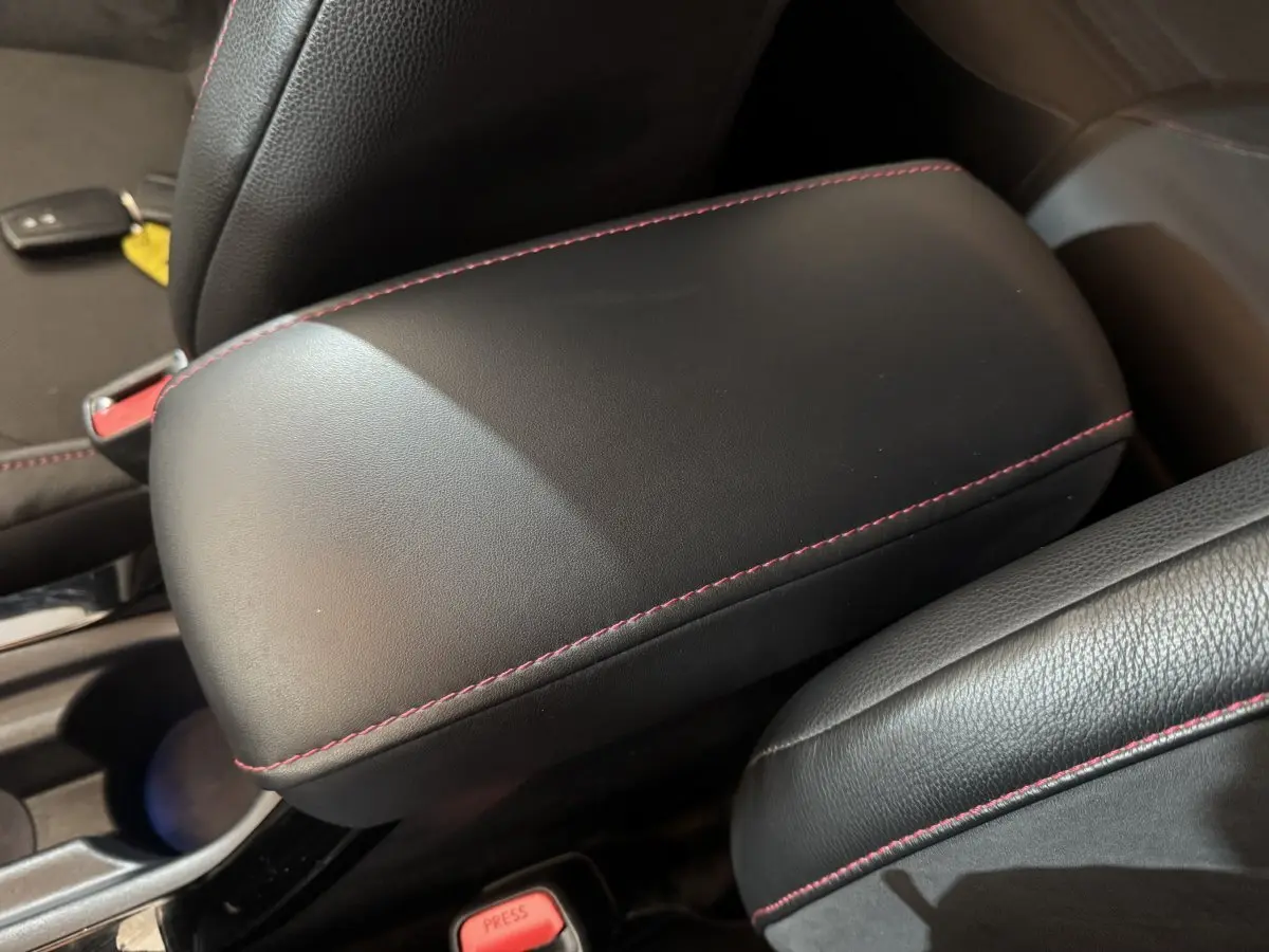 Détail de l'accoudoir central en cuir noir avec surpiqûres rouges dans l'habitacle d'une Toyota Corolla hybride.