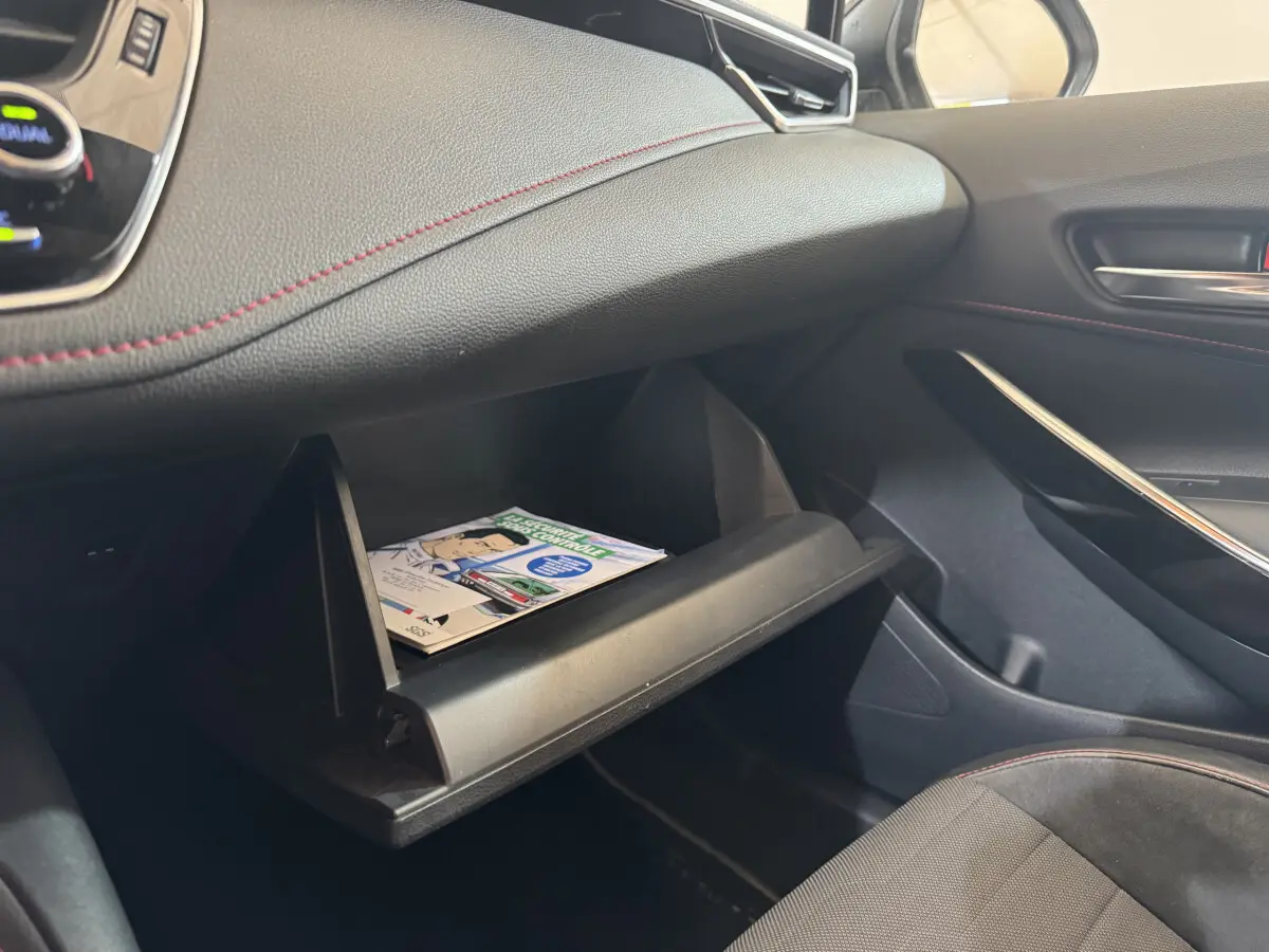 Intérieur côté passager de la Toyota Corolla hybride 2021, boîte à gants ouverte avec livret visible, sellerie noire.