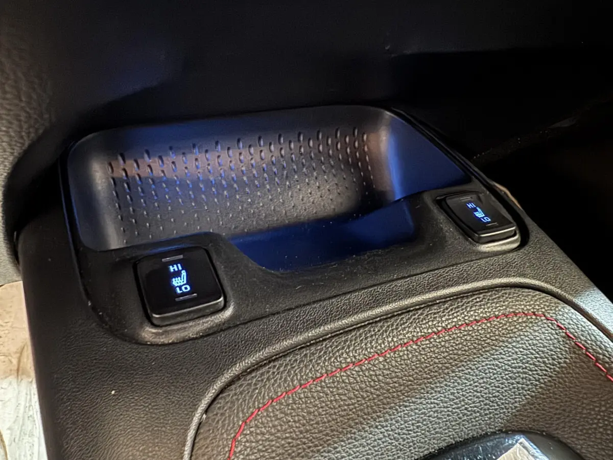 Gros plan sur les commandes de sièges chauffants avant, console centrale en cuir noir avec surpiqûres rouges, Toyota Corolla hybride.