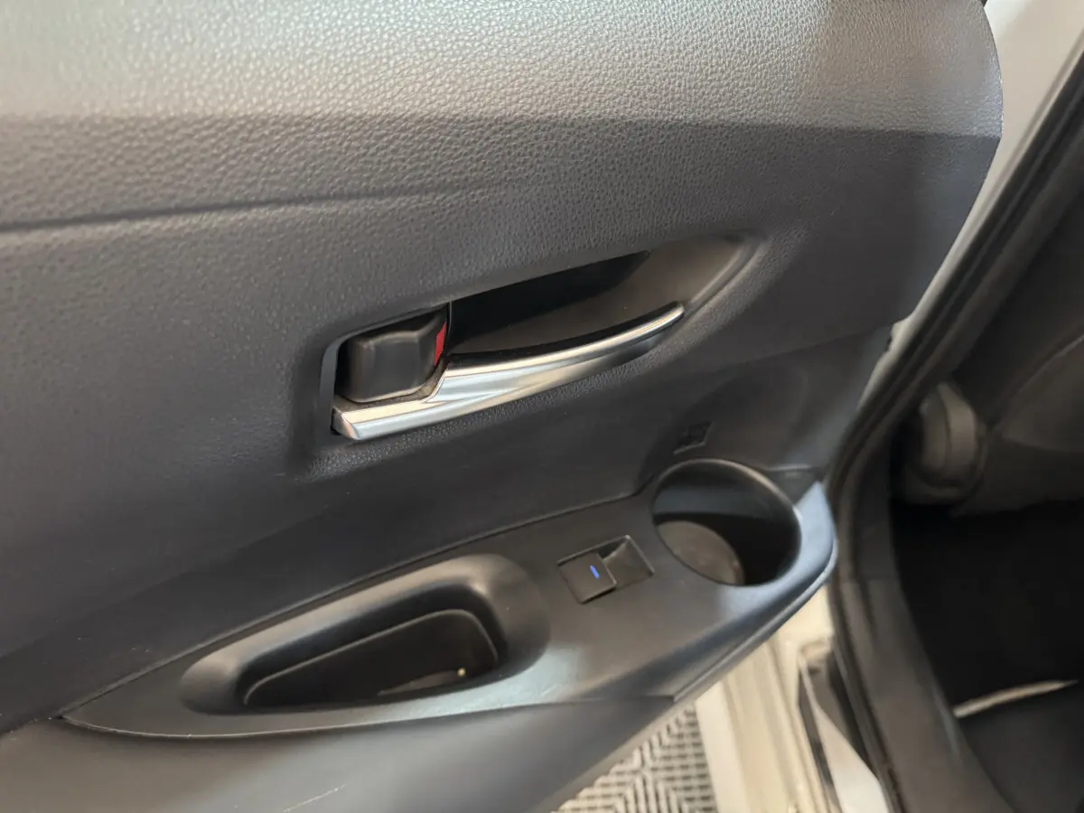 Gros plan sur la poignée intérieure et la commande de vitre de la porte avant gauche d'une Toyota Corolla hybride gris clair.