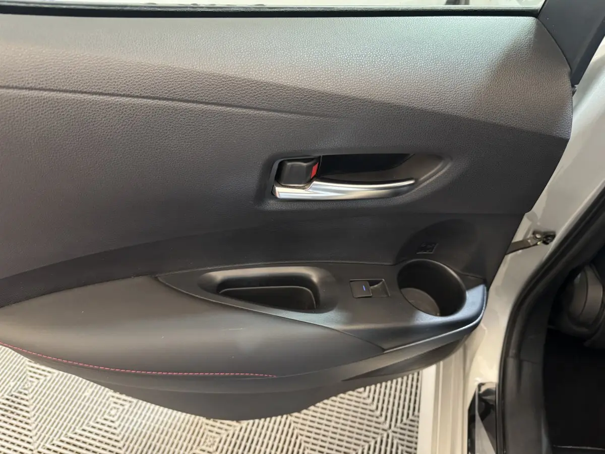 Vue rapprochée de la porte avant gauche grise de la Toyota Corolla Hybride 122h, avec poignée intérieure chromée et accoudoir noir.