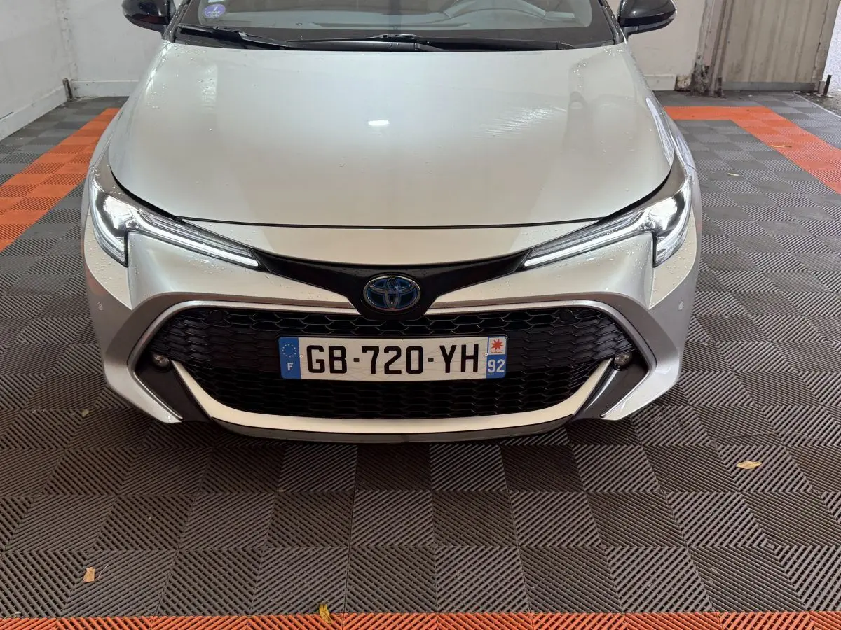 Vue avant rapprochée d'une Toyota Corolla Hybride 122h Collection gris clair avec calandre noire et phares LED fins.