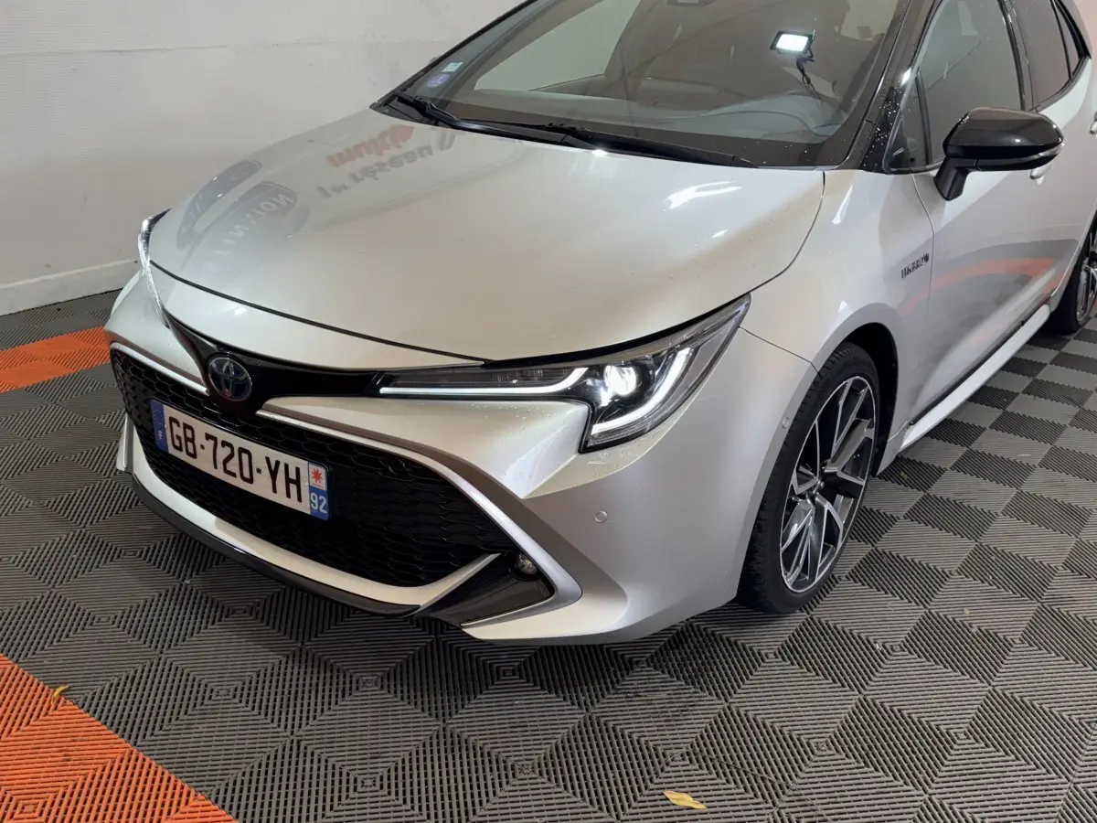 Vue 3/4 avant droit d'une Toyota Corolla Hybride 122h Collection gris clair avec phares LED allumés et jantes alliage.