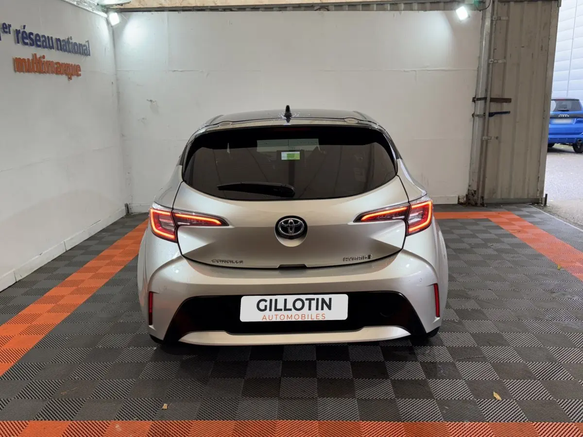 Vue arrière d'une Toyota Corolla Hybride gris clair avec feux LED allumés dans un garage.