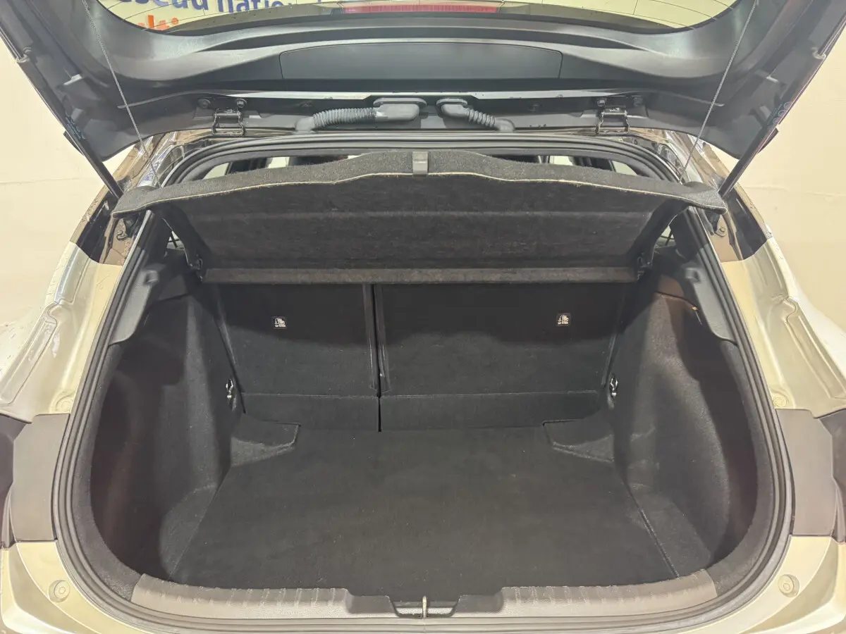 Coffre ouvert d’une Toyota Corolla hybride gris clair, vue arrière montrant l’espace de chargement vide et la tablette cache-bagages.