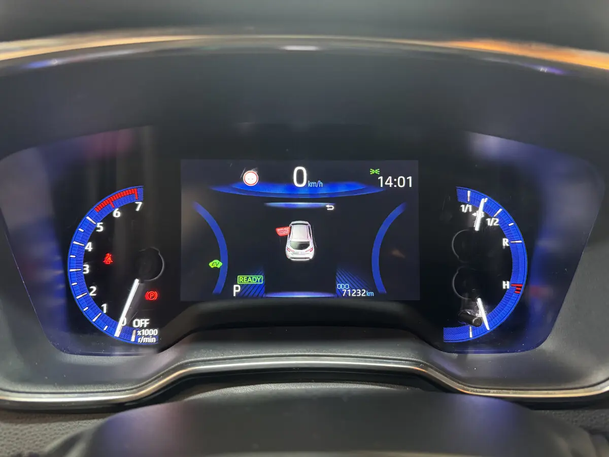 Vue rapprochée du tableau de bord numérique de la Toyota Corolla Hybride 122h gris clair, affichant 0 km/h et 71232 km.