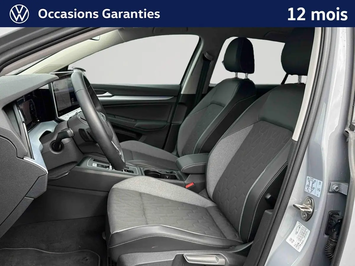 Intérieur avant droit d'une Volkswagen Golf grise 2025, sièges bi-matière gris et noir avec coutures apparentes.