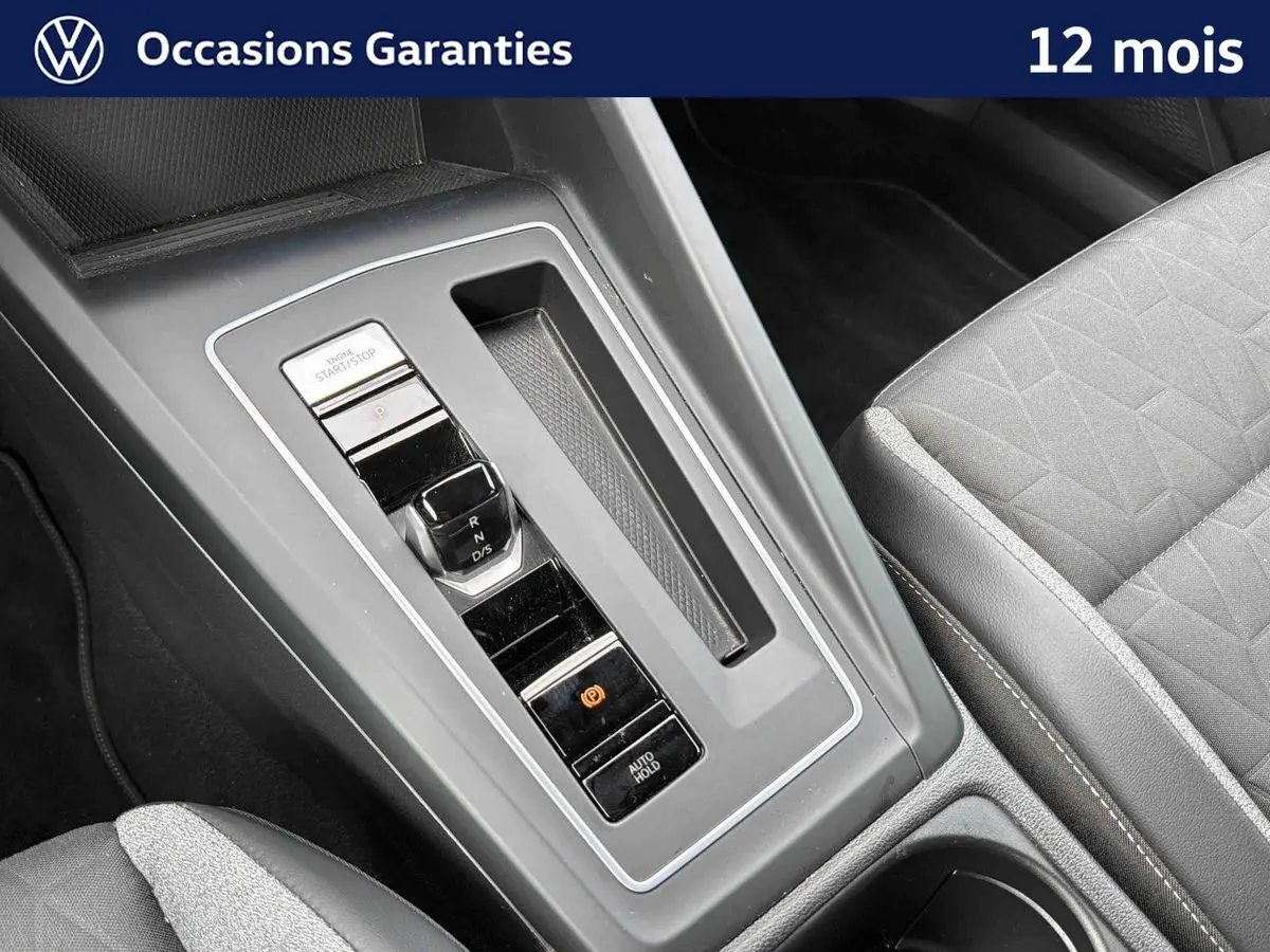 Gros plan sur la console centrale grise de la Volkswagen Golf 1.5 eTSI 2025 avec levier de vitesses et siège tissu gris.