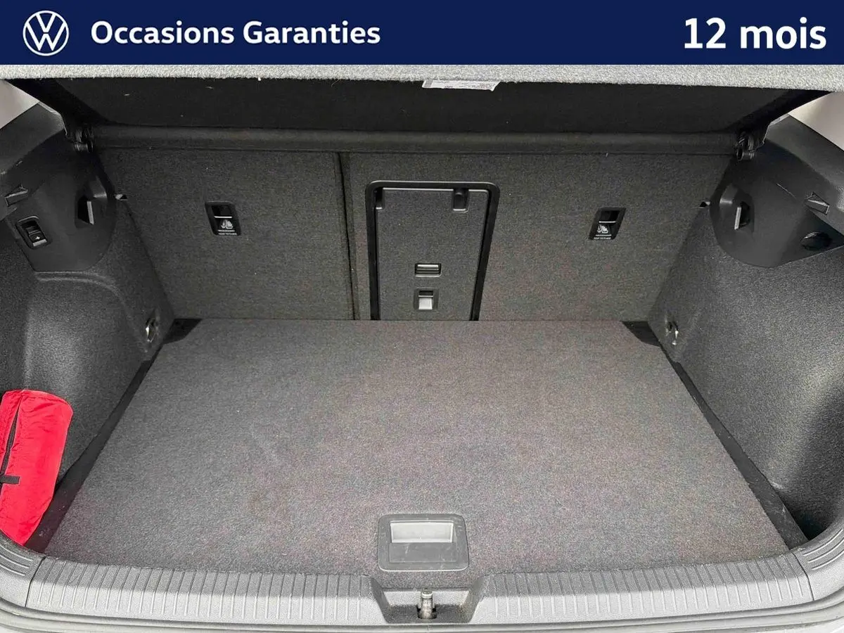 Coffre spacieux et propre d'une Volkswagen Golf 2025, vue de l'intérieur avec tapis gris et trousse de secours rouge.