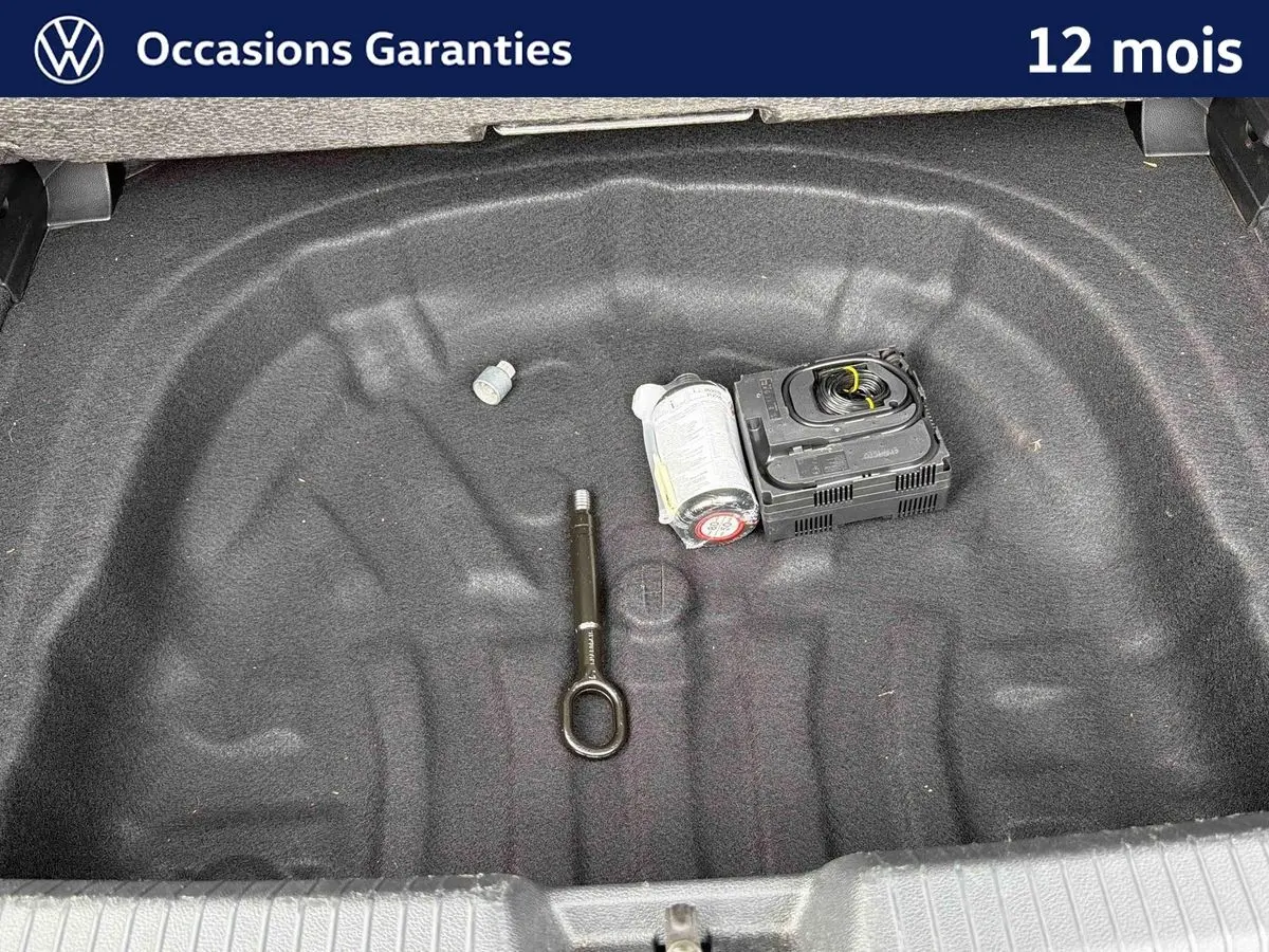 Vue plongeante sur le coffre ouvert d'une Volkswagen Golf grise, montrant un espace vide avec kit de réparation pneus.
