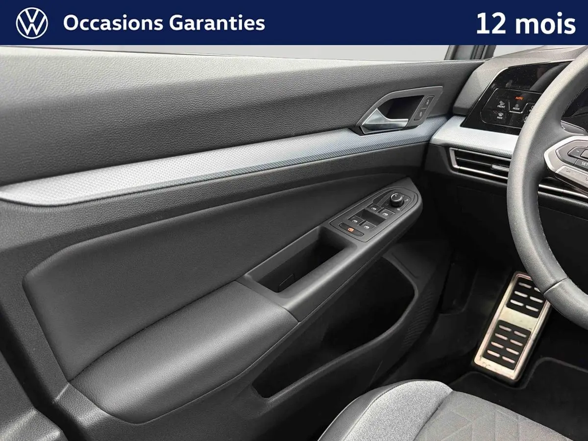 Intérieur côté conducteur de Volkswagen Golf gris, montrant la portière avec commandes électriques et partie du volant.