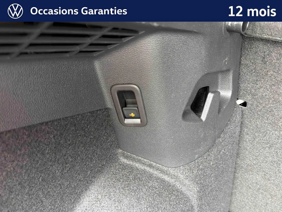 Détail du coffre d’une Volkswagen Golf grise montrant un levier de déverrouillage électrique du dispositif d’attelage.