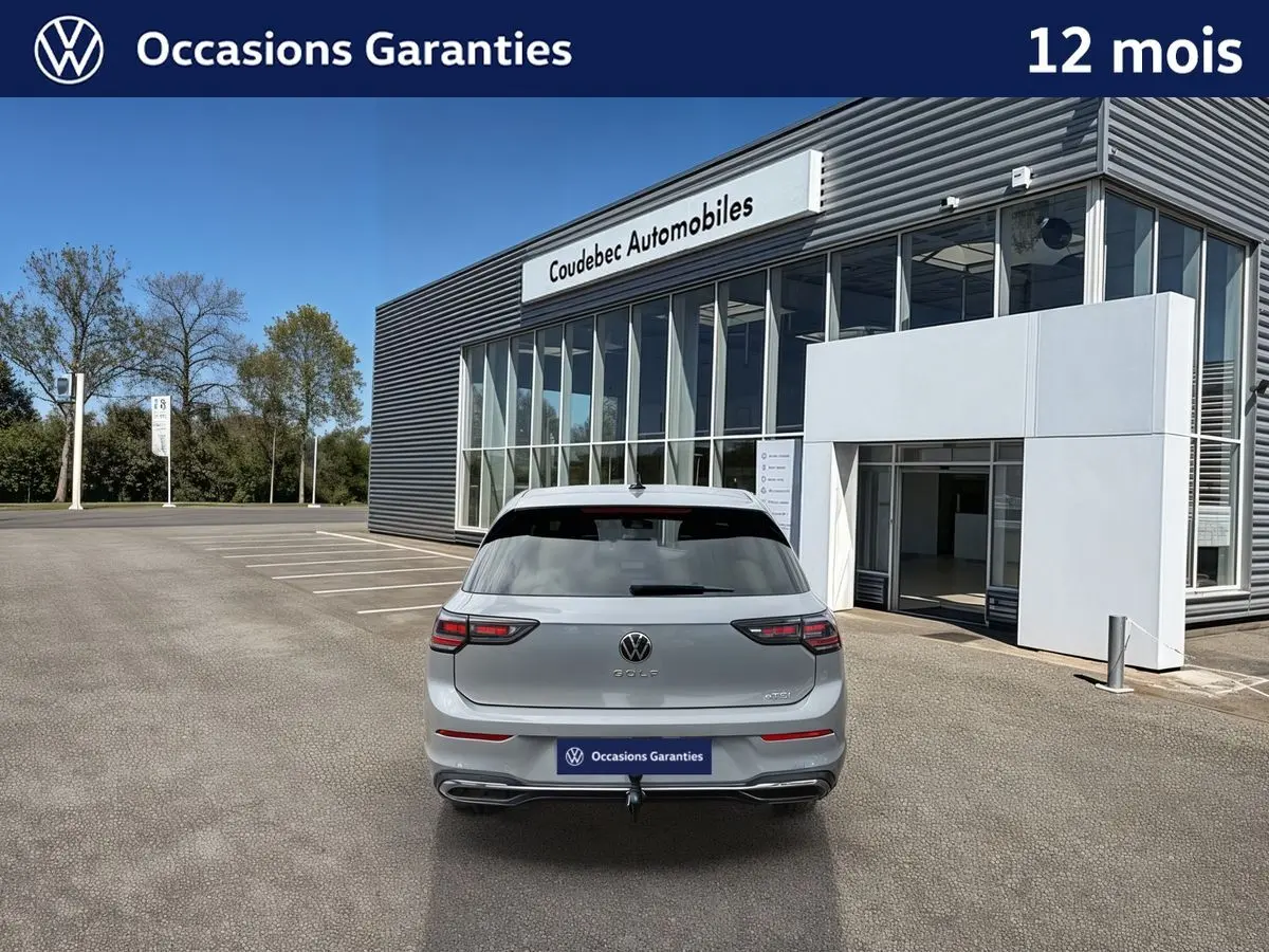 Vue arrière d'une Volkswagen Golf grise 2025 avec attelage escamotable, stationnée devant un bâtiment moderne.