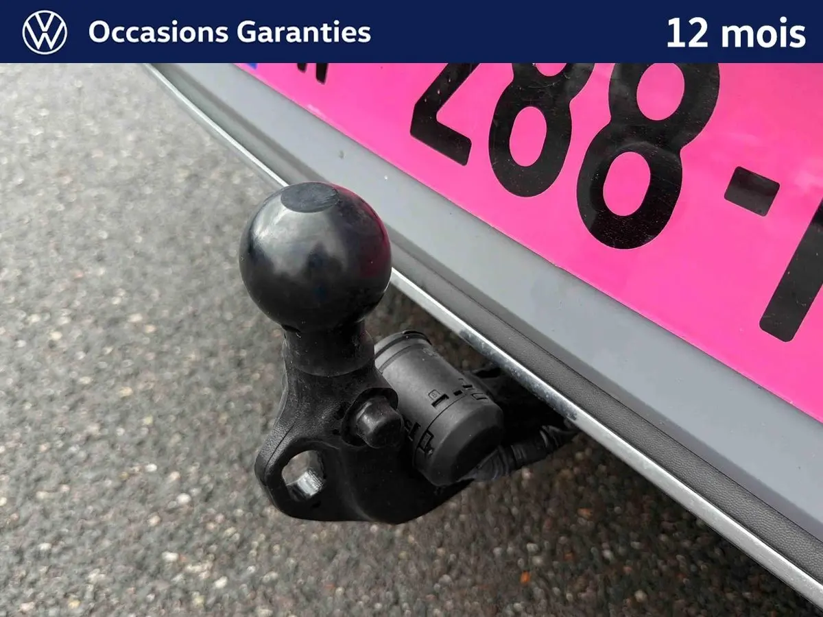 Gros plan sur l'attelage escamotable noir sous le pare-chocs arrière gris d'une Volkswagen Golf 2025.