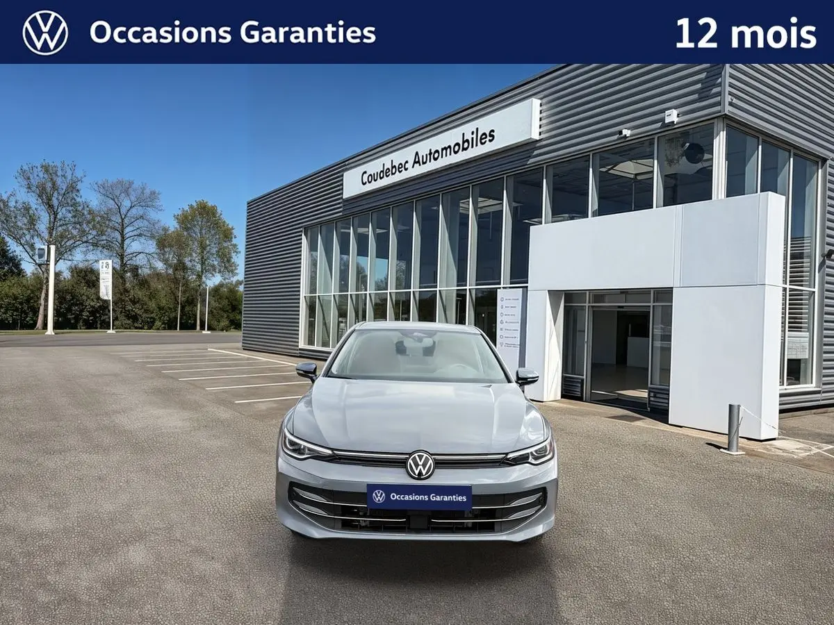 Vue frontale d'une Volkswagen Golf 1.5 eTSI grise stationnée devant un bâtiment moderne de concession automobile.