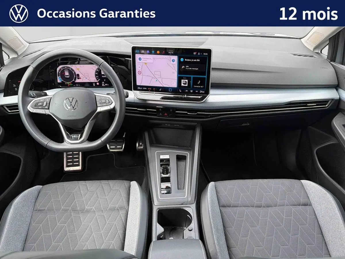 Vue intérieure avant de la Volkswagen Golf 1.5 eTSI 2025 avec tableau de bord digital et sièges gris à motifs géométriques.