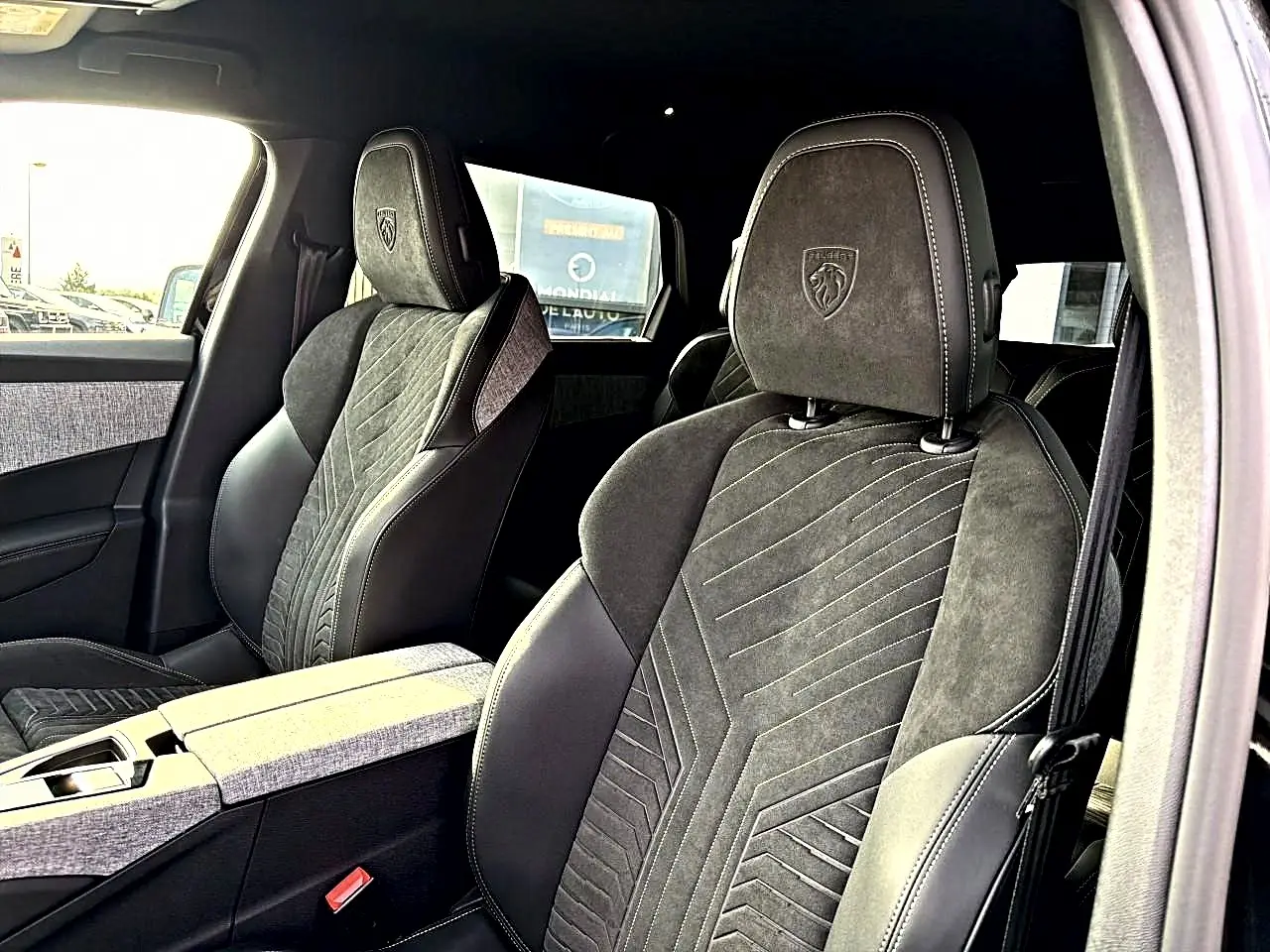 Vue intérieure des sièges avant noirs en cuir et alcantara du Peugeot 5008 Hybrid 145 GT, avec logo Peugeot brodé sur les appuis-tête.