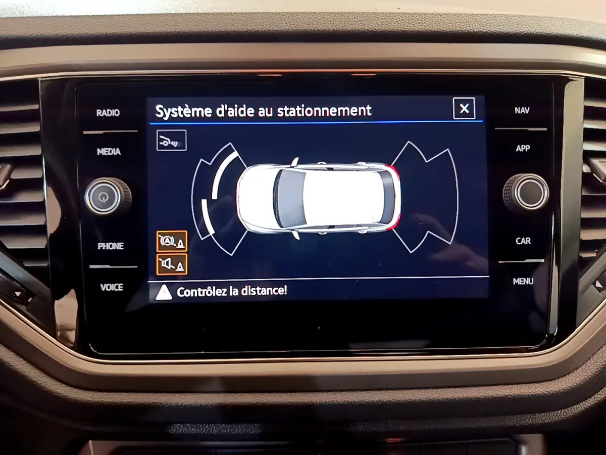 Écran tactile du système d'aide au stationnement montrant une vue aérienne du Volkswagen T-Roc gris foncé.