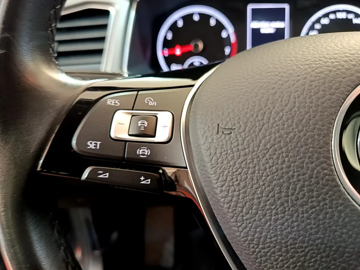 Gros plan sur les commandes du volant cuir noir du Volkswagen T-Roc 2021, avec tableau de bord numérique en arrière-plan flou.