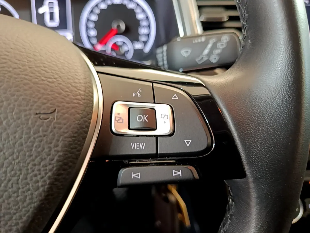 Gros plan sur les commandes au volant côté gauche du Volkswagen T-Roc gris foncé, avec tableau de bord en arrière-plan.