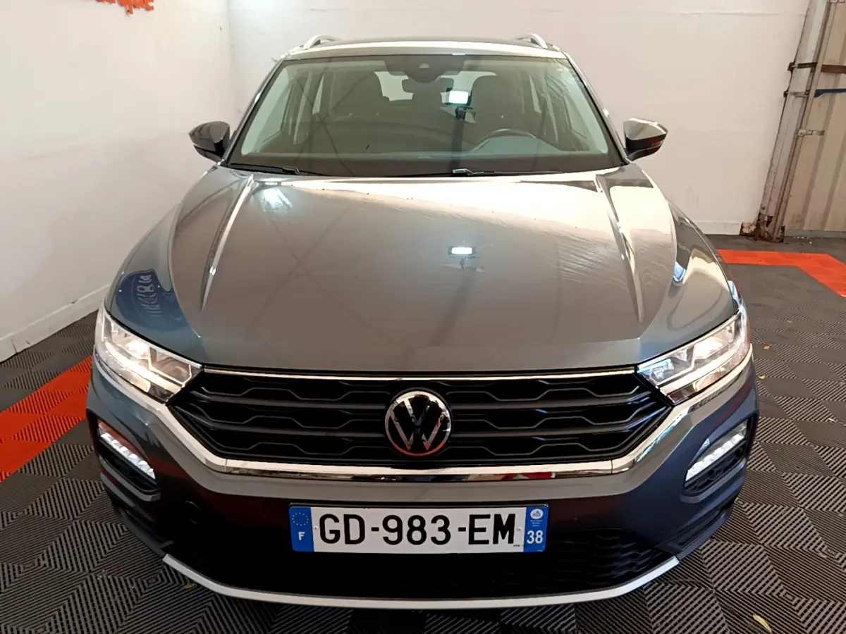 Vue avant d'un Volkswagen T-Roc gris foncé avec calandre noire et phares LED allumés dans un garage.