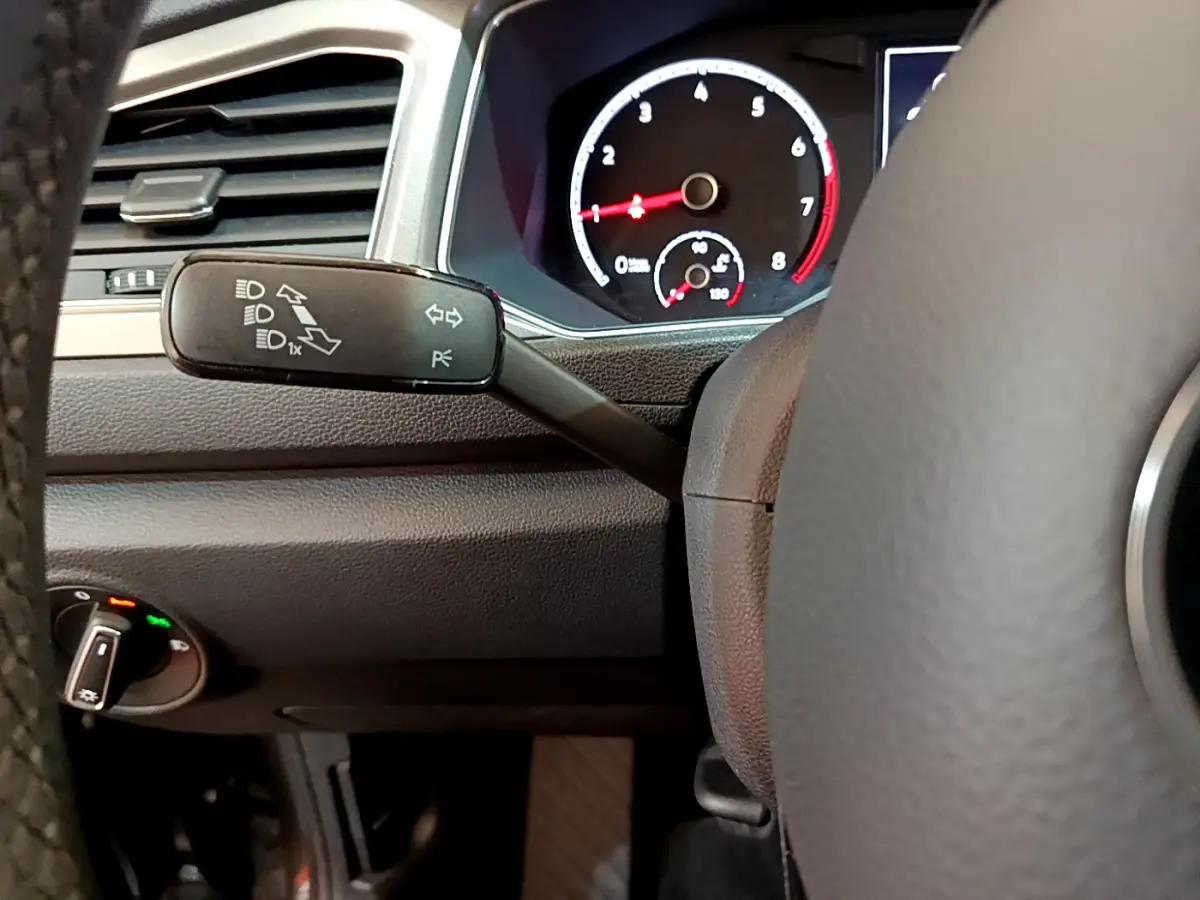 Détail intérieur du volant et levier de clignotant du Volkswagen T-Roc gris foncé, avec tableau de bord numérique visible.