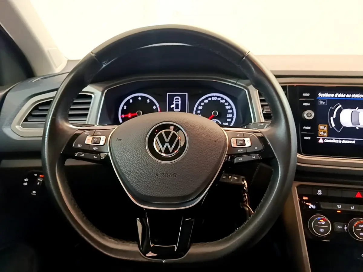 Vue intérieure centrée sur le volant cuir noir du Volkswagen T-Roc avec tableau de bord et écran tactile allumés.
