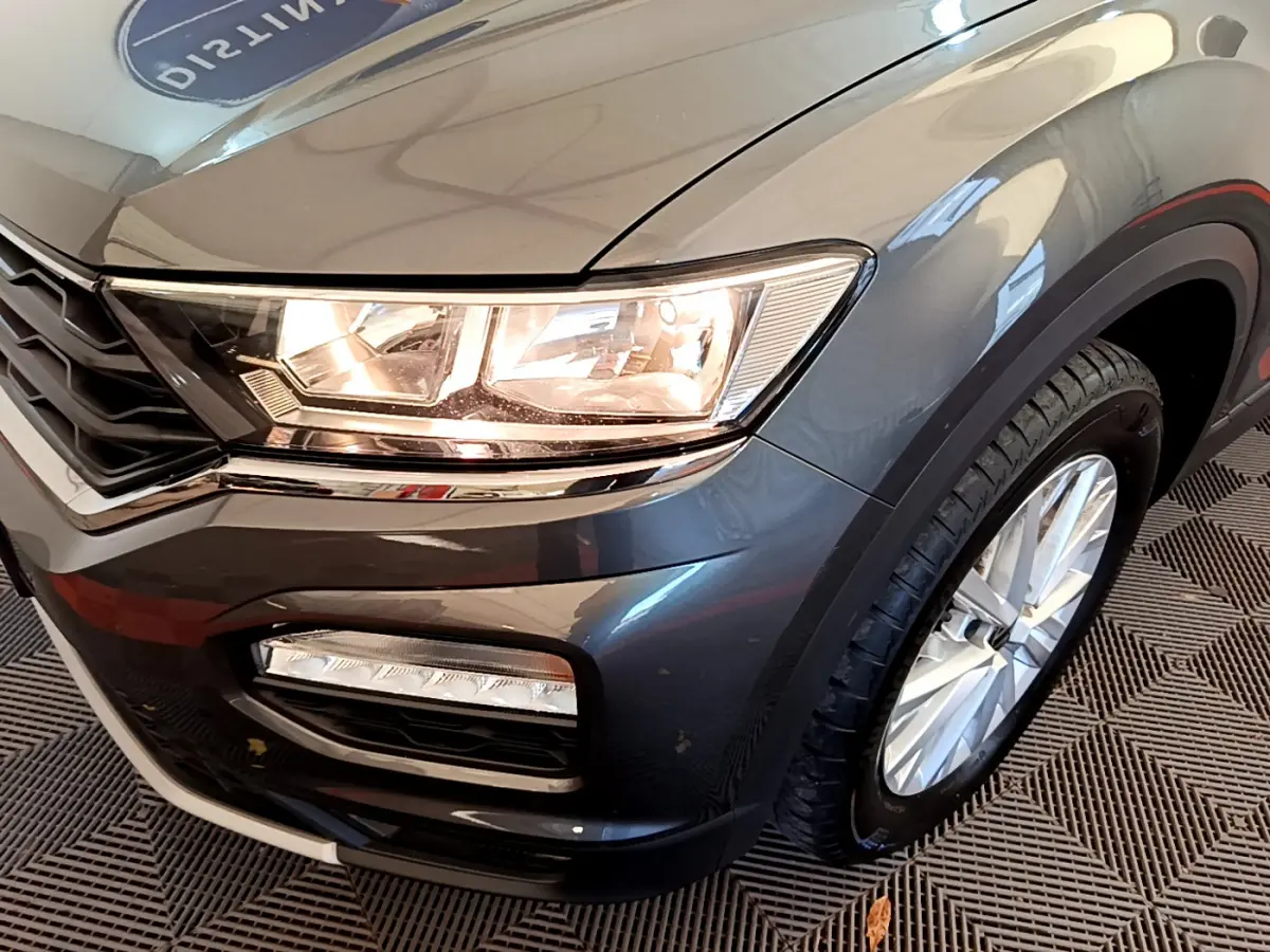 Gros plan sur l'avant droit d'un Volkswagen T-Roc gris foncé, mettant en valeur le phare et la roue.