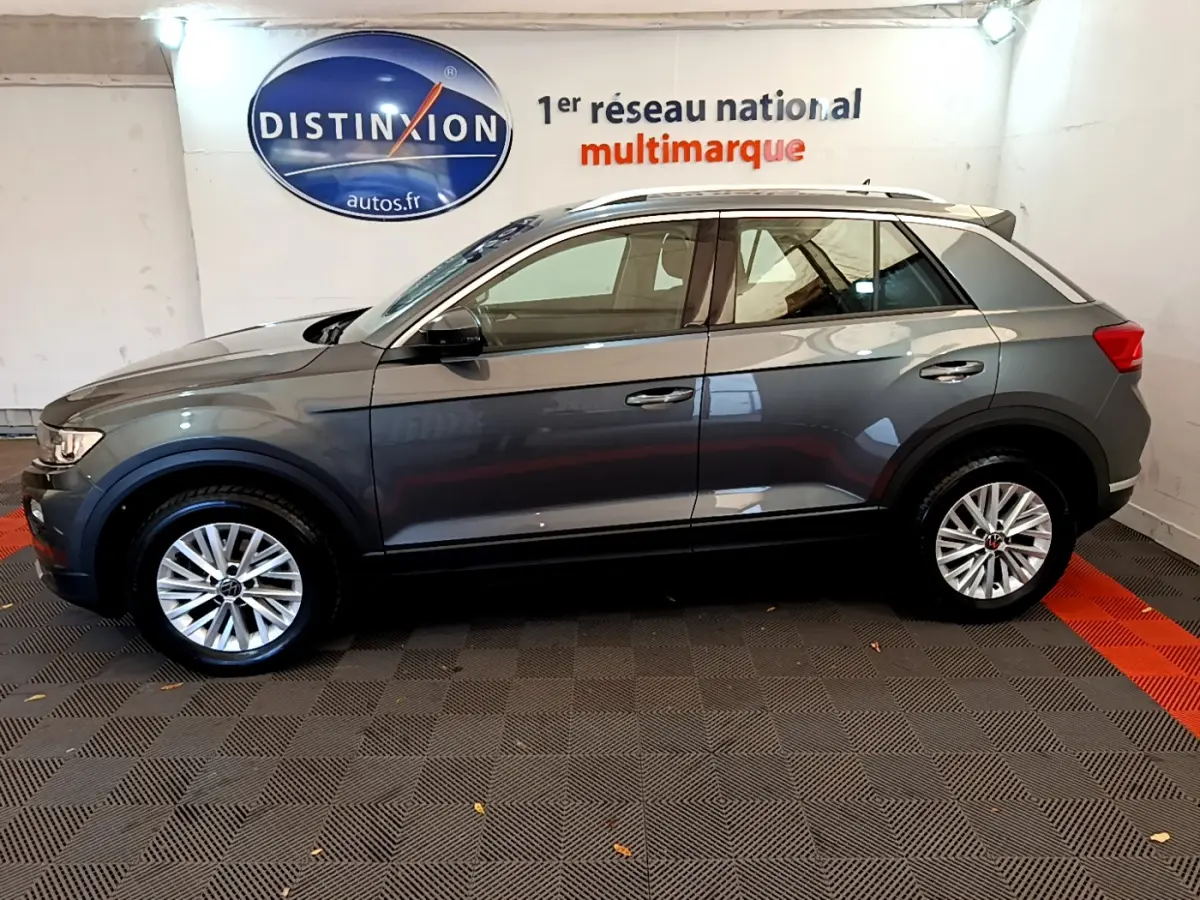 Vue de profil côté gauche d'un Volkswagen T-Roc gris foncé stationné en intérieur avec jantes argentées.