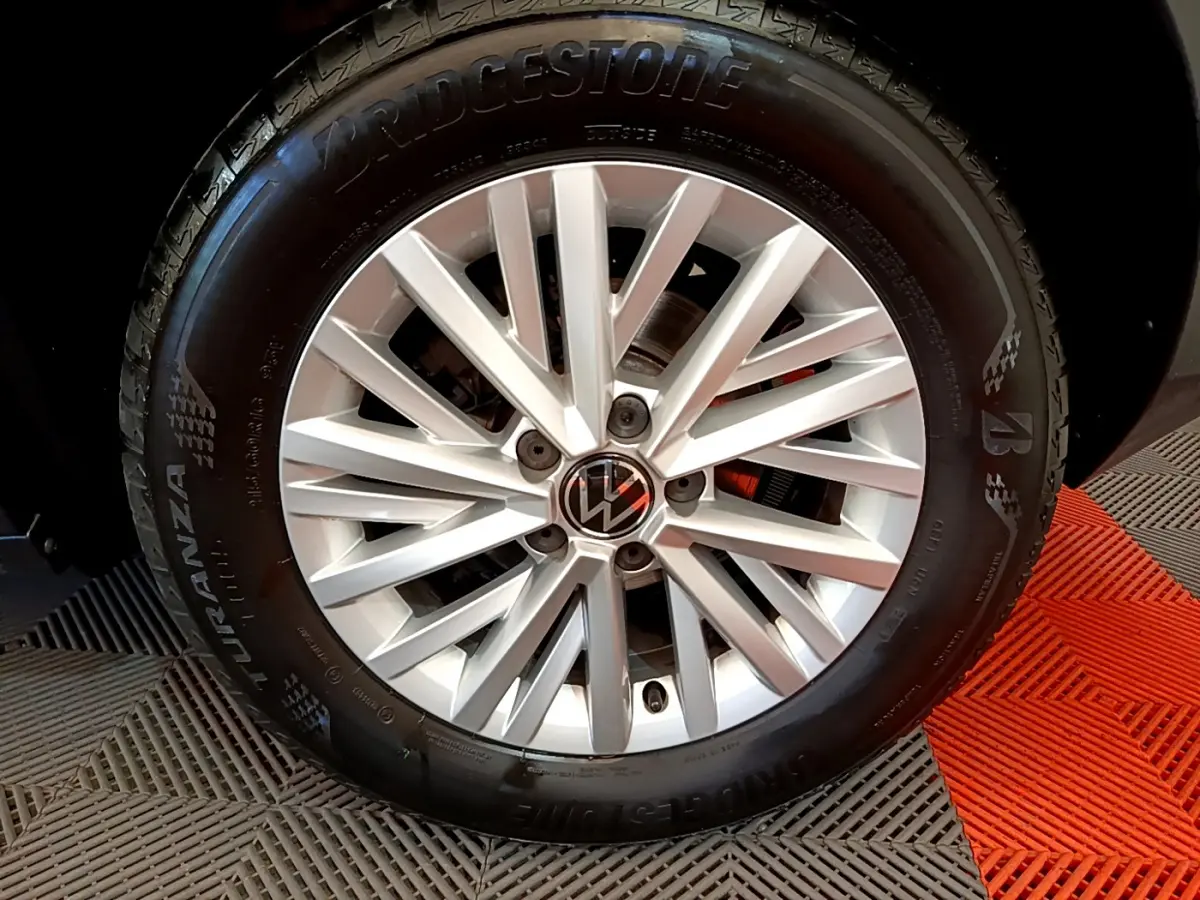 Gros plan sur la jante argentée avec logo Volkswagen du Volkswagen T-Roc gris foncé, pneu Bridgestone visible.