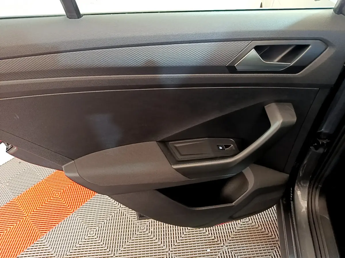 Vue rapprochée de la porte intérieure côté droit du Volkswagen T-Roc gris foncé, avec poignée et commande de vitre.