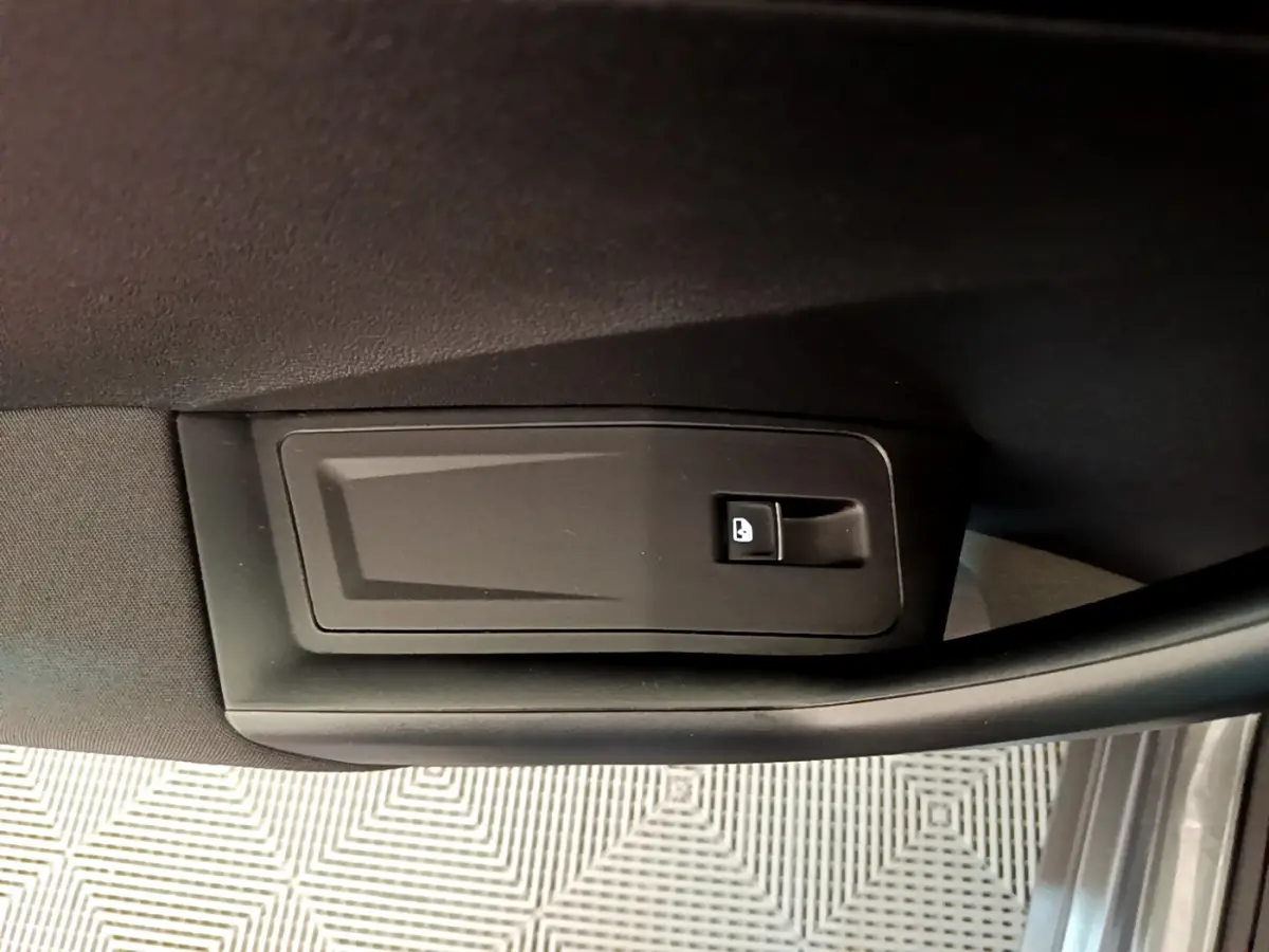 Gros plan sur le bouton d'ouverture de coffre intégré à la garniture intérieure de porte côté conducteur du Volkswagen T-Roc gris foncé.