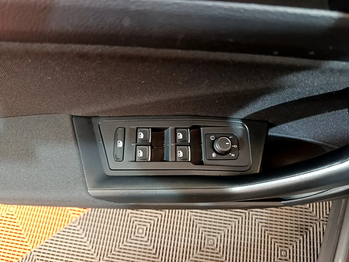 Vue rapprochée des commandes de lève-vitres et rétroviseurs sur la porte côté conducteur d'un Volkswagen T-Roc gris foncé.