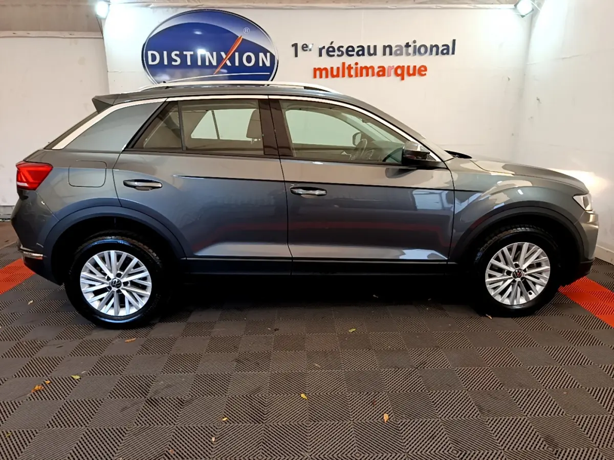 Volkswagen T-Roc gris foncé vue de profil côté gauche, avec jantes alliage et barres de toit noires.