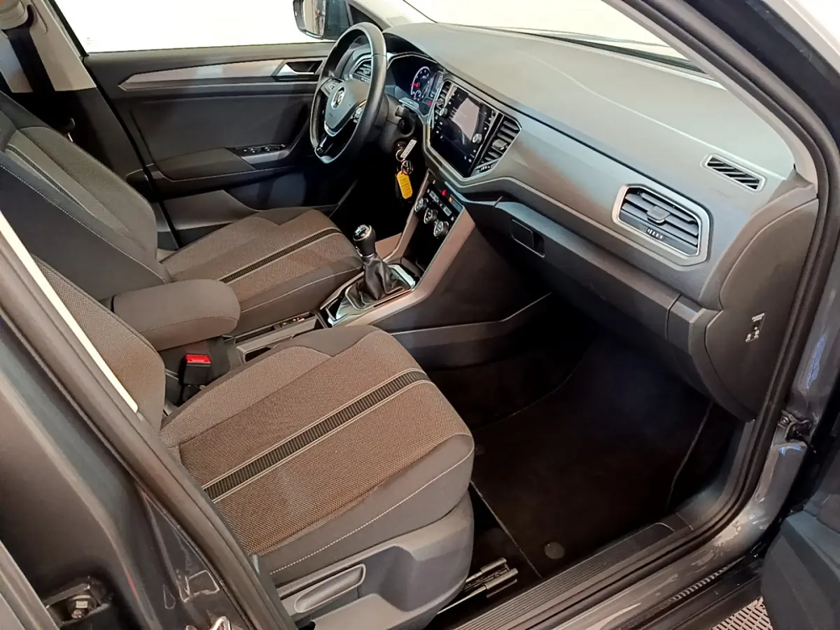 Vue intérieure côté passager du Volkswagen T-Roc gris foncé, montrant tableau de bord et sièges tissu avec console centrale.