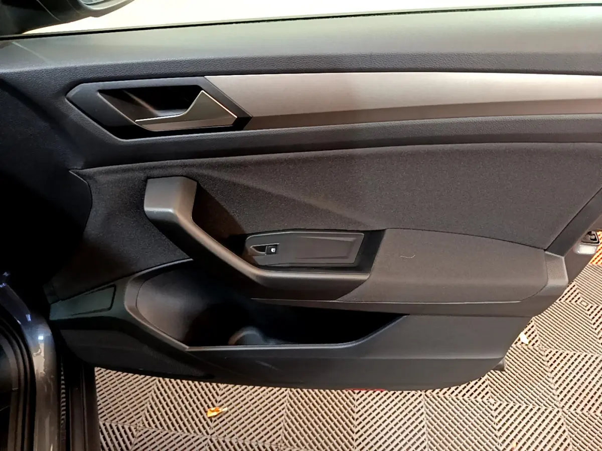 Vue intérieure du panneau de porte côté conducteur du Volkswagen T-Roc gris foncé, avec poignée et commande de vitre électrique.