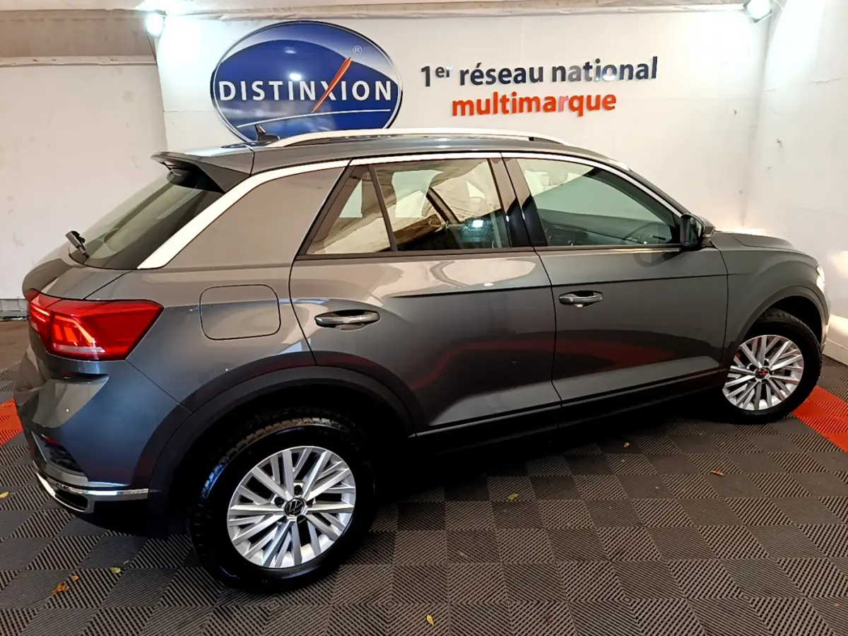 Vue latérale droite d'un Volkswagen T-Roc gris foncé avec toit blanc et jantes alliage en intérieur showroom.